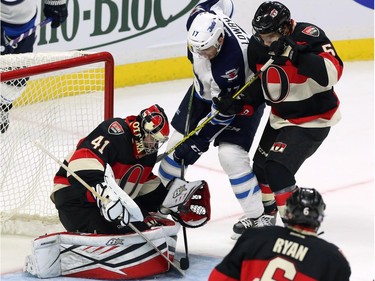 Ottawa Senators' goaltender Craig Anderson (41) attempts to grab the puck with his trapper as teammate Cody Ceci (5) and Winnipeg Jets' Adam Lowry (17) look on during second period NHL hockey action, in Ottawa, on Thursday, Nov. 5, 2015.