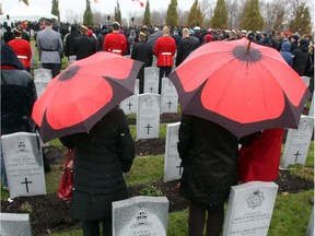 Members of the public stand in the falling wet snow with poppy motif umbrellas as they take part in Remembrance Day ceremonies at the Beechwood Military Cemetery in Ottawa, Monday, November 11, 2013.