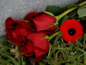 Roses and a poppy rest a the base of a headstone at the National Military Cemetery in Ottawa on Monday, November 10, 2014.