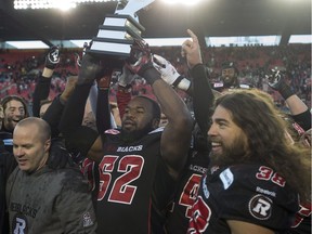 Ottawa Redblacks defensive lineman Shawn Lemon holds up the East Division trophy as he celebrates with linebacker James Green and coach Rick Campbell following their win over the Hamilton Tiger-Cats in the CFL East Division final Sunday, Nov. 22, 2015, in Ottawa.