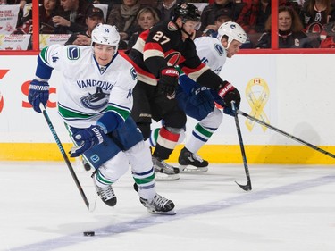 Alex Burrows #14 of the Vancouver Canucks stickhandles the puck as Curtis Lazar #27 of the Ottawa Senators and Derek Dorsett #15 skate up ice.