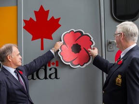 Yves Desjardins-Siciliano, President and CEO of VIA Rail, and Tom Eagles, Dominion President of the Legion place a poppy decal on the side of a train engine as they gathered at the Ottawa train station.