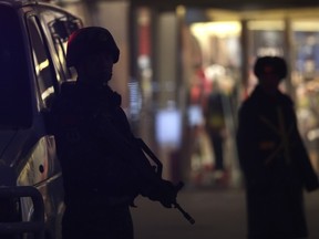 A security guard patrol past an armed Chinese paramilitary policeman stands watch in the capital city's popular shopping and nightlife area of Sanlitun during a heightened security alert in Beijing, Tuesday, Dec. 29, 2015. Two Chinese men were detained in a southern Chinese city for spreading a rumor that hundreds of terrorists have arrived in the city, local police said, just days before a new law banning false terror information goes into effect.