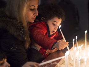 Newly-arrived Syrian refugee Ani Movsisyan, left, and her two-year-old son Michael Yanikian light a candle after meeting up with relatives at the Armenian Community Centre in Toronto on Wednesday, December 16, 2015.