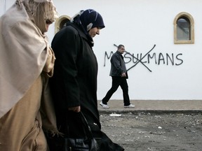 In this Monday Feb. 8, 2010 file photo, Muslim residents walk past racial slurs painted on the walls of a mosque in the town of Saint-Etienne, central France. Graffiti reads: "Muslims".