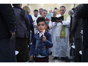 In this Thursday, Dec. 24, 2015 photo, a boy dressed in a tiny denim suit jacket as Iraqi Christians celebrate during Christmas Eve mass in the Al-Bashara Church in a Christian refugee camp in Irbil, northern Iraq. Many of the worshippers are displaced from their homes after Islamic State militants swept through northern Iraq in 2014.
