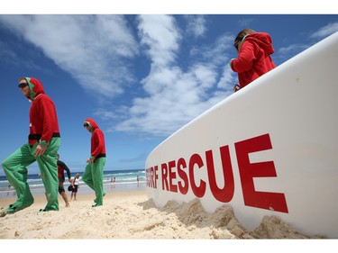 James Conaghan, left, of Australia in Santa's elves costume, walks past a surf rescue board on Bondi Beach with relatives from Ireland Ross and Sarah Conaghan, right, while celebrating Christmas Day in Sydney, Australia, Friday, Dec. 25, 2015.