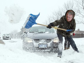 Sander Kruger, right, tries to clear a path for his car while his wife, Alicia, left, looks on on Cambridge St. S at Bronson Ave after a heavy snowfall hit the capital region Tuesday December 29, 2015.