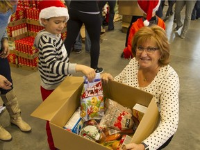 Susan Anson, with some help from five-year-old Dylan Malhotra, fills a food hamper. Long ago a recipient of a similar hamper, Anson has for the past three years returned the favour, delivering the supplies to the less fortunate.