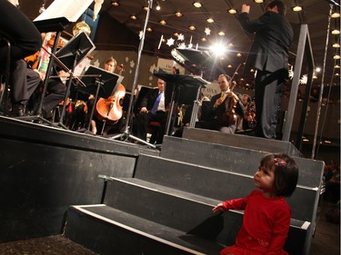 Two-year-old Hanako Kawasaki watches from her own front row seat as her violin-playing parents, Jessica Linnebach and Yosuke Kawasaki, perform during the free annual Christmas FanFair Concert presented by the National Arts Centre Orchestra Players' Association, at the NAC on Sunday, December 13, 2015.