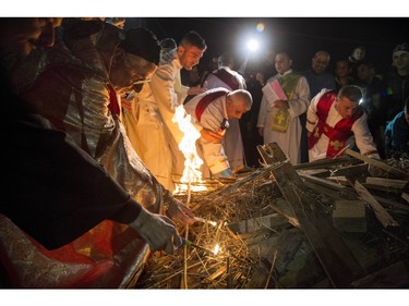 In this Thursday, Dec. 24, 2015 photo, Assiryan-Catholic Archbishop of Mosul, Youhanna  Boutros Moshe, second left, lights the holy fire during Christmas Eve mass in the Al-Bashara Church in a Christian refugee camp in Irbil, northern Iraq. Many of the worshippers are displaced from their homes after Islamic State militants swept through northern Iraq in 2014.