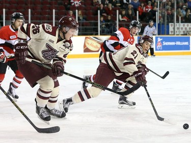 Austen Keating #9 of the Ottawa 67's looks on as Jonathan Ang #21 and Josh Coyle #26 of the Peterborough Petes skate after the loose puck.