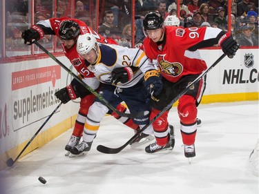 Zack Smith #15 and Alex Chiasson #90 of the Ottawa Senators squeeze Johan Larsson #22 of the Buffalo Sabres off the puck.
