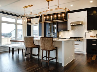 The kitchen and family room in the St. James are one large space, so Kinkade designed them to complement each other. Black and white cabinetry offers impact with the walnut island and the dark wood floor adding warmth and gold hardware and oversized lanterns making dramatic accents. The crisp white quartz counter and simple subway tile keep the space cleanly tailored.