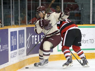 Jonathan Ang #21 of the Peterborough Petes gets the puck past a checking Chase Campbell #39 of the Ottawa 67's.