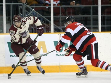 Jonathan Ang #21 of the Peterborough Petes stickhandles the puck against Chase Campbell #39 of the Ottawa 67's.