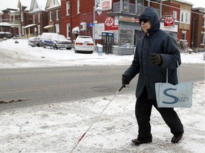 Ricardo Ng uses a white cane to help guide his way along Preston Street near Elm Street during Thursday's snowfall.