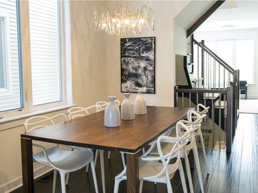 A modern and stylish dining room greets visitors entering the Ruby town, where a warm walnut table is paired with graphic white entangled dining chairs and a wire dining fixture.