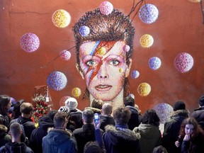 TOPSHOT - Crowds gather to read and place floral tributes beneath a mural of British singer David Bowie, painted by Australian street artist James Cochran, aka Jimmy C, following the announcement of Bowie's death, in Brixton, south London, on January 11, 2016. British music icon David Bowie died of cancer at the age of 69, drawing an outpouring of tributes for the innovative star famed for groundbreaking hits like "Ziggy Stardust" and his theatrical shape-shifting style.