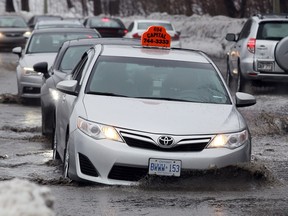 A taxi falls into a large pothole covered by water on Colonel By Drive.