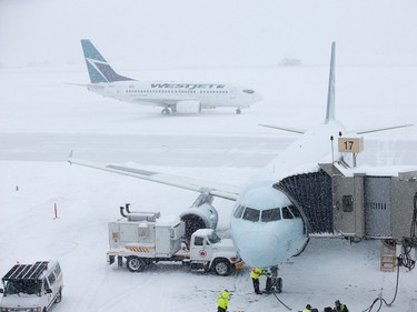 A West Jet aircraft taxis on the runway while an Air Canada plane loads passengers as the region deals with a major snow storm.