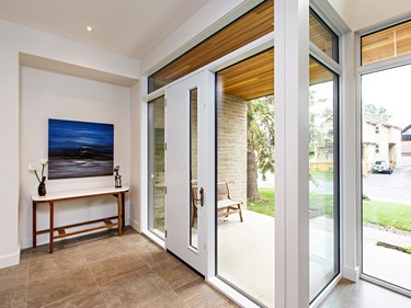 The bright foyer with its transom windows connects the home's interior with the outside world. An inset on the far wall repeats the foyer's strongly linear design and frames the painting and table.