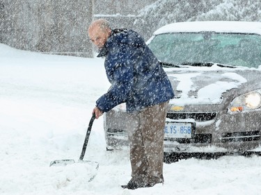 An elderly man tries to dig the roadway out, blocking his car off Carling Avenue Tuesday.