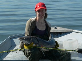 Fabienne Côté of Petit Brûlé sits in her boat on the St. Lawrence River with a just-caught sturgeon.