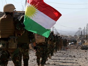 Iraqi autonomous Kurdish region's Peshmerga forces and fighters from the Yazidi minority, a local Kurdish-speaking community which the Islamic State (IS) group had brutally targeted in the area, hold a Kurdish flag while entering the northern Iraqi town of Sinjar, in the Nineveh Province, on November 13, 2015.