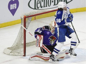 Syracuse Crunch player Tye McGinn is hit by the puck as he screens Binghamton Senators goalie Chris Driedger on Saturday, Feb. 13, 2016. The DIFD logo is visible on the boards and on the front of Driedger's jersey.