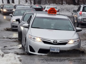 A taxi falls into a large pothole covered by water along a flooded Colonel By Dr, near the Bank St. bridge, in Ottawa, Ont. Thursday February 25, 2016. Wide-spread flooding occurred across the city after a heavy rainfall.