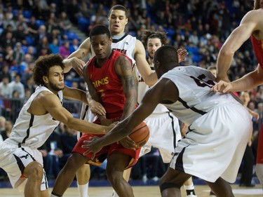 Calgary Dinos' Thomas Cooper, centre, loses control of the ball while being pressured by Carleton Ravens' Kaza Kajami-Keane, left, and Ryan Ejim, right, during CIS men's national university basketball championship final game action in Vancouver, B.C., on Sunday March 20, 2016.