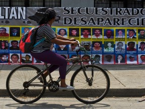 A woman rides her bicycle in front of a banner with pictures of missing persons in Cali, Colombia, in the dispute between the government and Farc rebels.