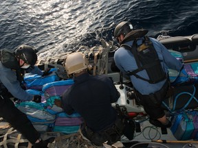 Sailors from Her Majesty's Canadian Ship (HMCS) EDMONTON and a United States Coast Guard Law Enforcement Detachment member (center) gather several packages that were recovered after being thrown overboard from a vessel of interest during Operation CARIBBE on March 25, 2016. Photo: OP Caribbe, DND