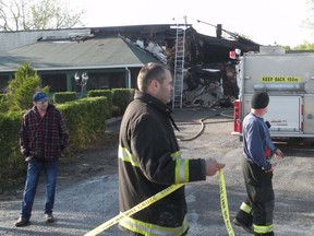 Bonnie Glen Pavilion owner Michel Diotte, left, watches as North Glengarry firefighters clean up the scene Friday morning following a fire that began Thursday night.