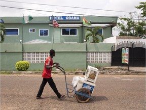 In this picture taken on Saturday, July 4, 2015, an ice cream vendor walks by a hotel named after U.S. President Barak Obama in Accra, Ghana. (AP Photo/Christian Thompson)