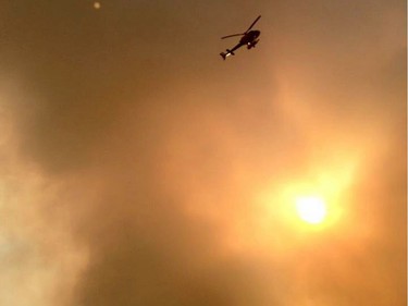 Smoke fills the air as a helicopter flies overhead in Fort McMurray, Alberta on Tuesday May 3, 2016. Raging forest fires whipped up by shifting winds sliced through the middle of the remote oilsands hub city of Fort McMurray Tuesday, sending tens of thousands fleeing in both directions and prompting the evacuation of the entire city.