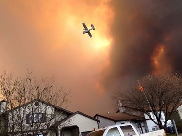 Smoke fills the air as a small plane flies overhead in Fort McMurray, Alberta on Tuesday May 3, 2016. Raging forest fires whipped up by shifting winds sliced through the middle of the remote oilsands hub city of Fort McMurray Tuesday, sending tens of thousands fleeing in both directions and prompting the evacuation of the entire city.