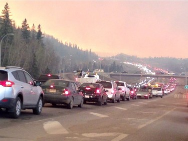 Smoke fills the air as cars line up on a road in Fort McMurray, Alberta on Tuesday May 3, 2016 in this image provide by radio station CAOS91.1. At least half of the city of Fort McMurray in northern Alberta was under an evacuation notice Tuesday as a wildfire whipped by winds engulfed homes and sent ash raining down on residents.