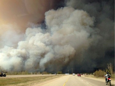 Smoke fills the air as people drive on a road in Fort McMurray, Alberta on Tuesday May 3, 2016 in this image provide by radio station CAOS91.1. At least half of the city of Fort McMurray in northern Alberta was under an evacuation notice Tuesday as a wildfire whipped by winds engulfed homes and sent ash raining down on residents.