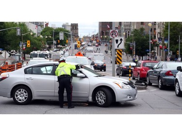 A police officer directs traffic on Elgin St late in the afternoon after sink hole occurred on Rideau St., June 08, 2016.  Photo by Jean Levac 
keyword: sinkhole Rideau Street