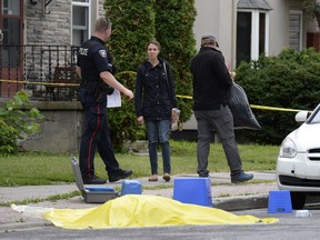 An Ottawa Police officer leads non-involved individuals, believed to be residents, from a home inside the crime scene of a homicide in Lowertown on July 10.