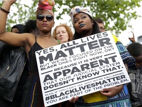 Two women hold a placard with the slogan "Yes, all lives matter" as people gather in Brixton, south London to protest against police brutality in the US, on July 9, 2016, after two recent incidents where black men have been shot and killed by police officers. /
