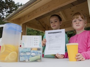 Eliza Andrews, 7, left, and her sister Adela Andrews, 5, hold their new special permit from the National Capital Commission allowing them to sell lemonade on Colonel By Drive as long as the proceeds are given to charity.