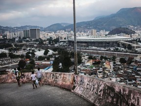 RIO DE JANEIRO, BRAZIL - JUNE 18:  People walk, with Maracana stadium in the background, in the Mangueira 'favela' community on June 18, 2016 in Rio de Janeiro, Brazil. Much of the Mangueira favela community sits about a kilometer away from Maracana stadium, which will be the site of the opening and closing ceremonies for the Rio 2016 Olympic Games. The stadium has received hundreds of millions of dollars in renovations ahead of the World Cup and Olympics. The Morar Carioca plan to urbanize Rio's favelas, or unplanned settlements, by 2020, was one key social legacy project heralded ahead of the Rio 2016 Olympic Games. The plan has mostly failed to materialize. Around 1.4 million residents, or approximately 22 percent of Rio's population, reside in favelas which often lack proper sanitation, health care, education and security due to gang and police violence.