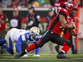 Winnipeg Blue Bombers' Brendan Morgan, left, looks on as Calgary Stampeders' Jerome Messam runs the ball during first half CFL football action in Calgary, Friday, July 1, 2016.
