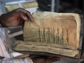 A man holds an ancient manuscript that will need to be restored after being damaged in Bamako, Mali, Tuesday, Jan. 27, 2015. After being saved from destruction at the hands of Islamic extremists, thousands of ancient manuscripts from the fabled northern Mali city of Timbuktu now face a less dramatic but still worrying threat: weather and poor storage conditions in their new location that scholars say could lead to permanent damage.