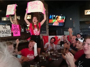 Katherine Dobson stands on a booth at the Glen Pub in Stittsville, cheering as her friend Erica Wiebe takes gold in women's wrestling on Thursday.