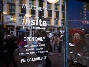 People are reflected in the window of supervised injection site, Insite, during a demonstration calling for more safe injection sites, in the Downtown Eastside of Vancouver, B.C., on Wednesday June 8, 2016. Two drug users' advocacy groups are calling on the B.C. government to open more safe injection sites to help prevent fatal overdoses.