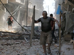 TOPSHOT - A Syrian man covered with dust carries pieces of metal on a street cluttered with rubble following a reported air strike on the rebel-held neighbourhood of Sakhur in the northern city of Aleppo, on August 15, 2016. /